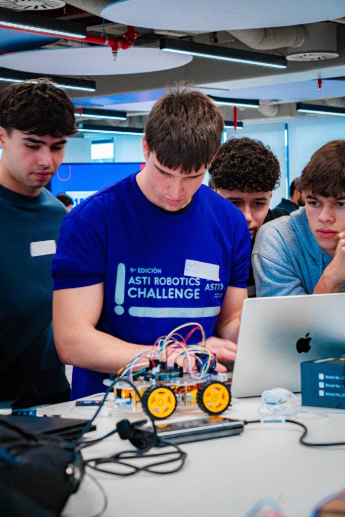 Un grupo de jóvenes participa en un desafío de robótica, trabajando en un proyecto con un robot y una laptop.