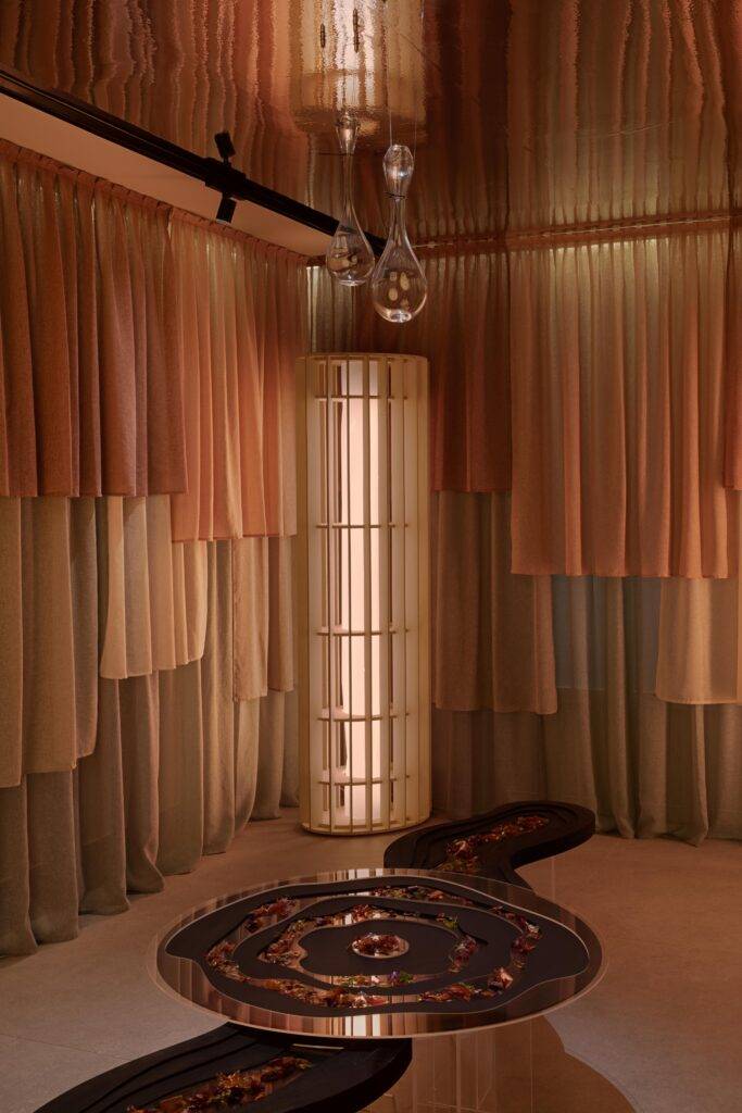 La imagen muestra un interior elegante con cortinas de tonos suaves y una mesa decorativa en el centro.