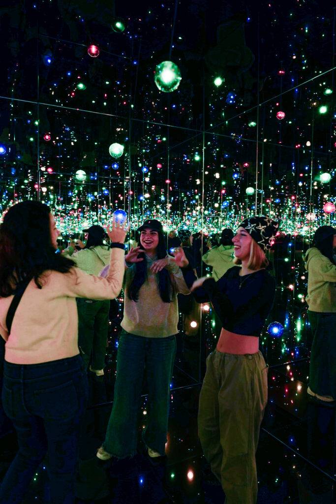 Tres amigas se divierten en una sala de espejos llenos de luces de colores.