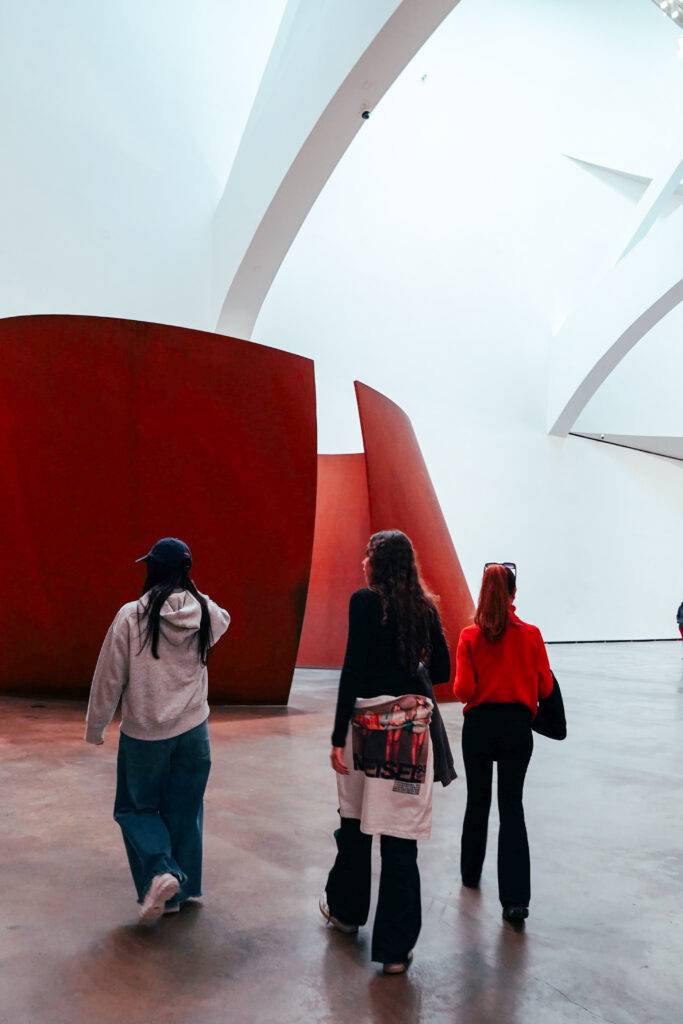 Tres personas caminan por un espacio moderno y luminoso con formas arquitectónicas interesantes.