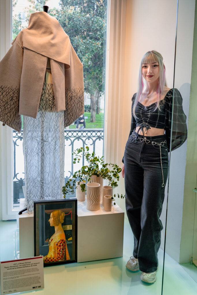 Una joven posa junto a una prenda de ropa en una exposición de moda.