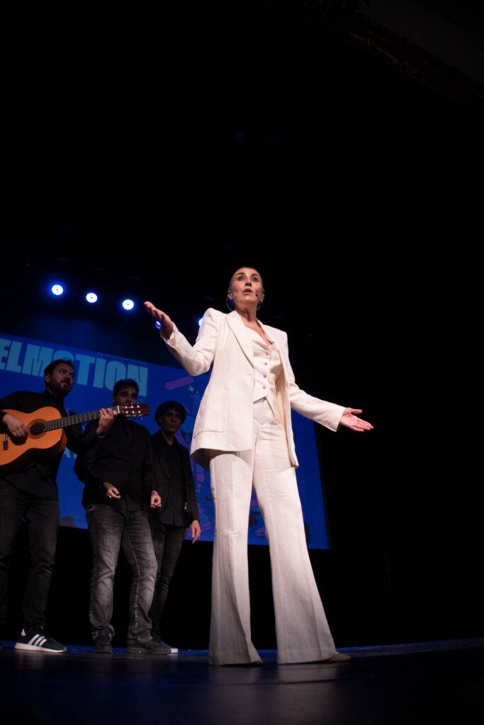 Una mujer vestida de blanco actúa en un escenario frente a un grupo de músicos.