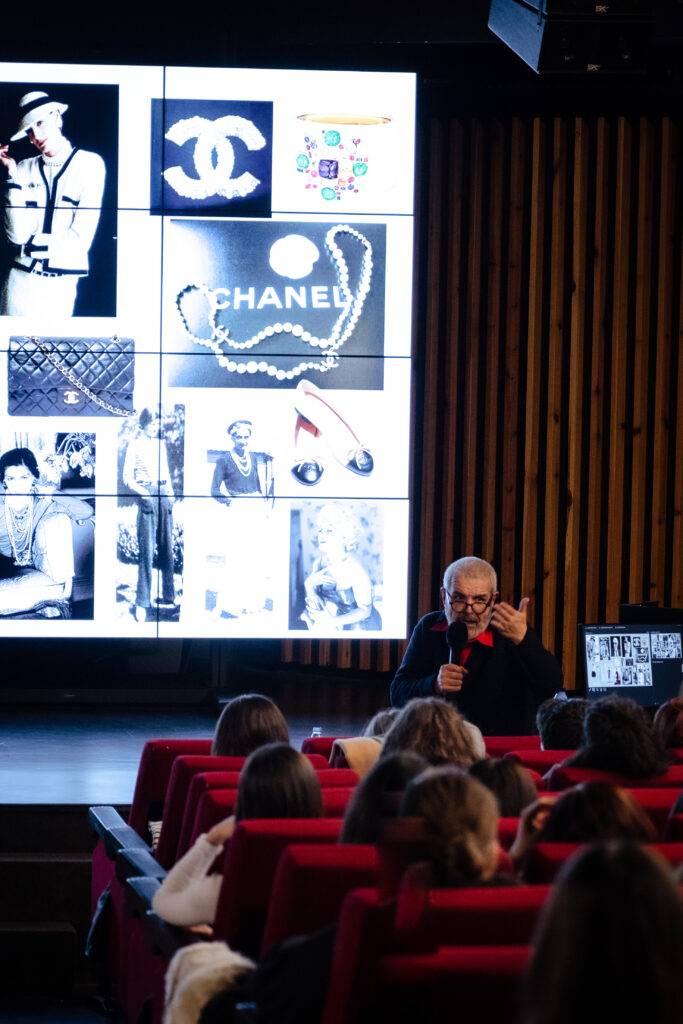 Una conferencia sobre la historia de la moda con imágenes de Chanel y un ponente en el escenario.