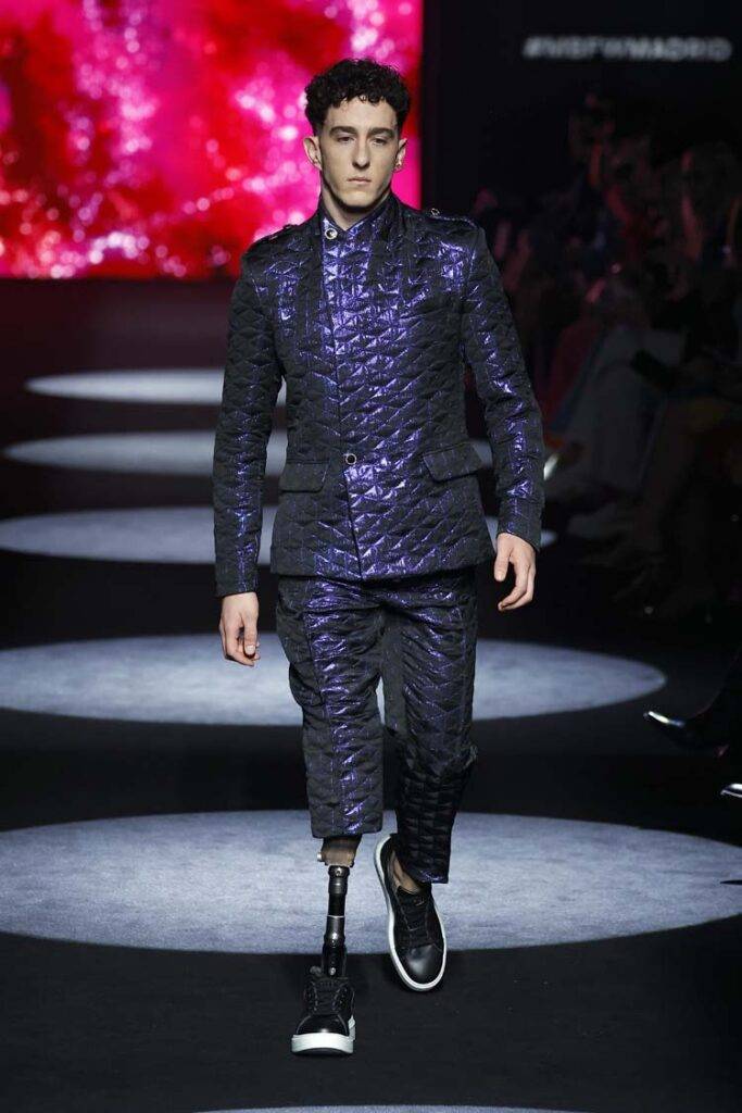 Un modelo camina por la pasarela luciendo un traje brillante y moderno.