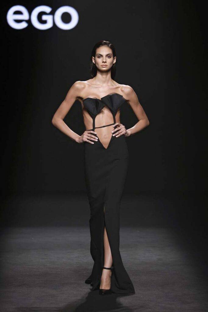 Una modelo camina por la pasarela luciendo un vestido negro elegante y atrevido.