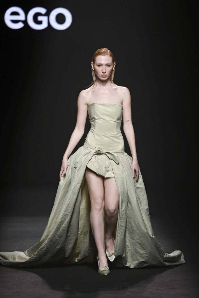 Una modelo presenta un vestido elegante y asimétrico en una pasarela oscura.