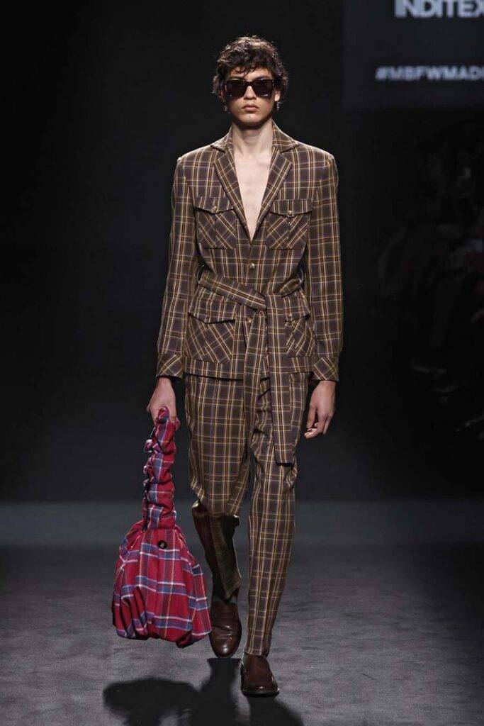 Modelo walk en la pasarela con un traje de cuadros y gafas de sol.