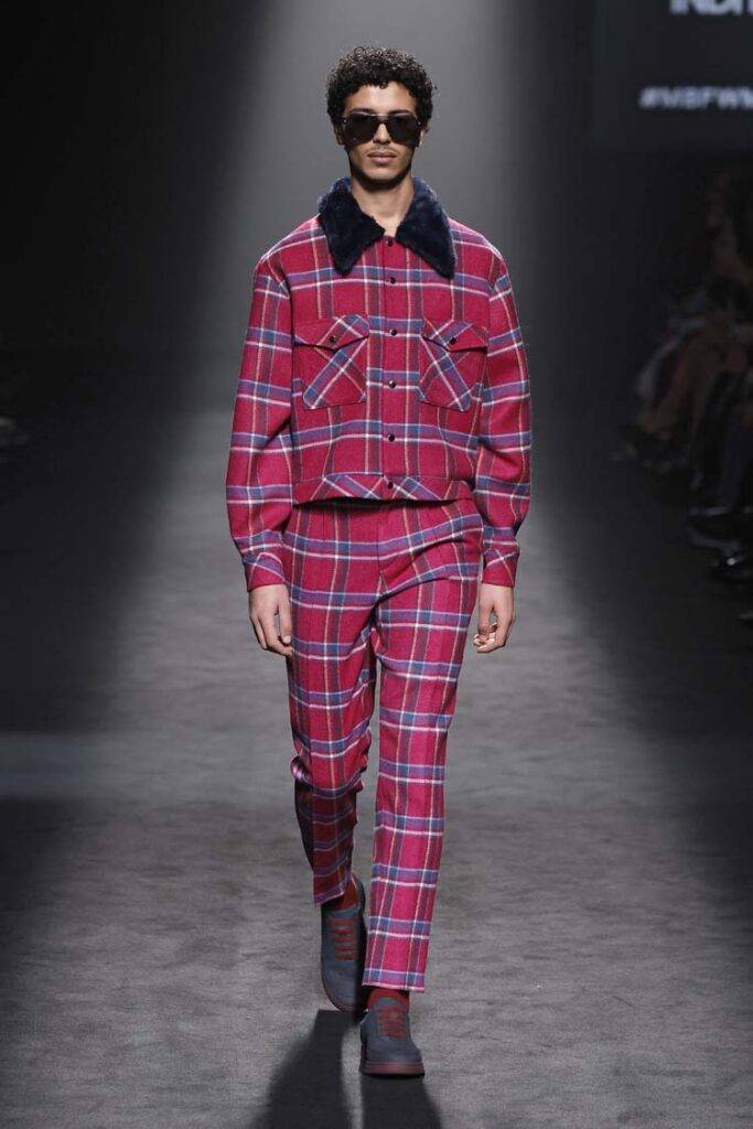 Un modelo camina por la pasarela luciendo un traje a cuadros en tonos rojos y azules.