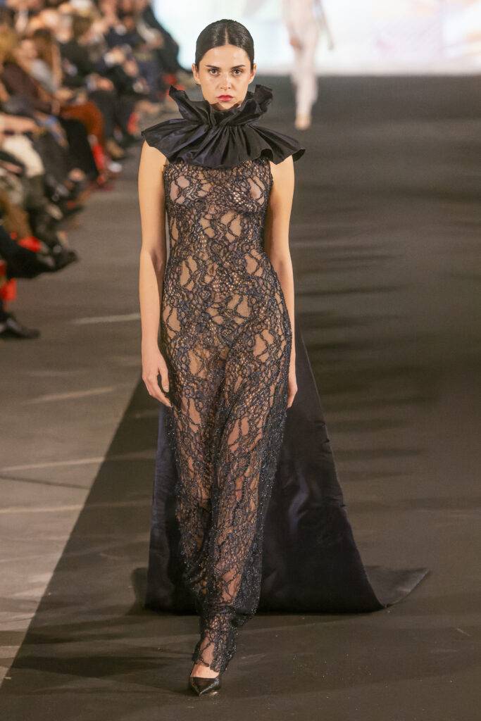 Modelo luciendo un vestido de encaje negro con un diseño elegante en una pasarela de moda.