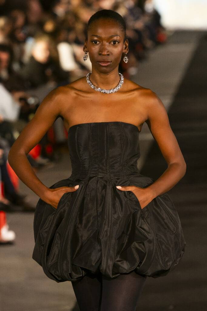 Una modelo luce un vestido negro sin mangas en una pasarela de moda.