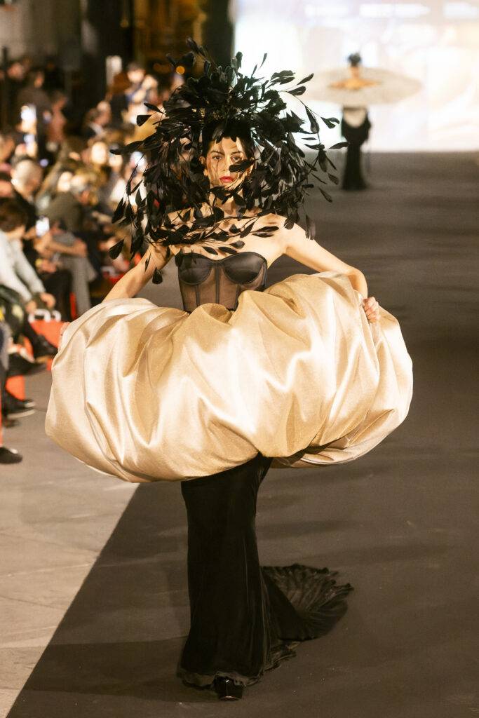 Una modelo camina por la pasarela con un vestido llamativo y un gran tocado de plumas.