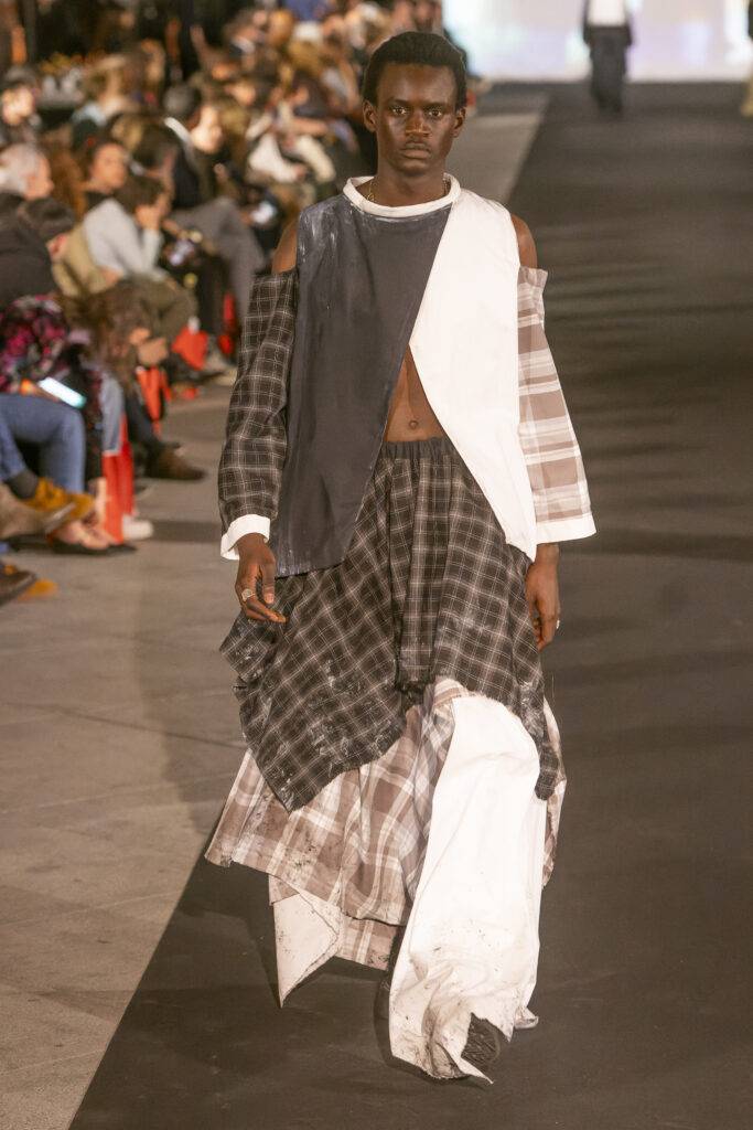 Un modelo masculino exhibe un conjunto de ropa de diseño creativo en una pasarela de moda.