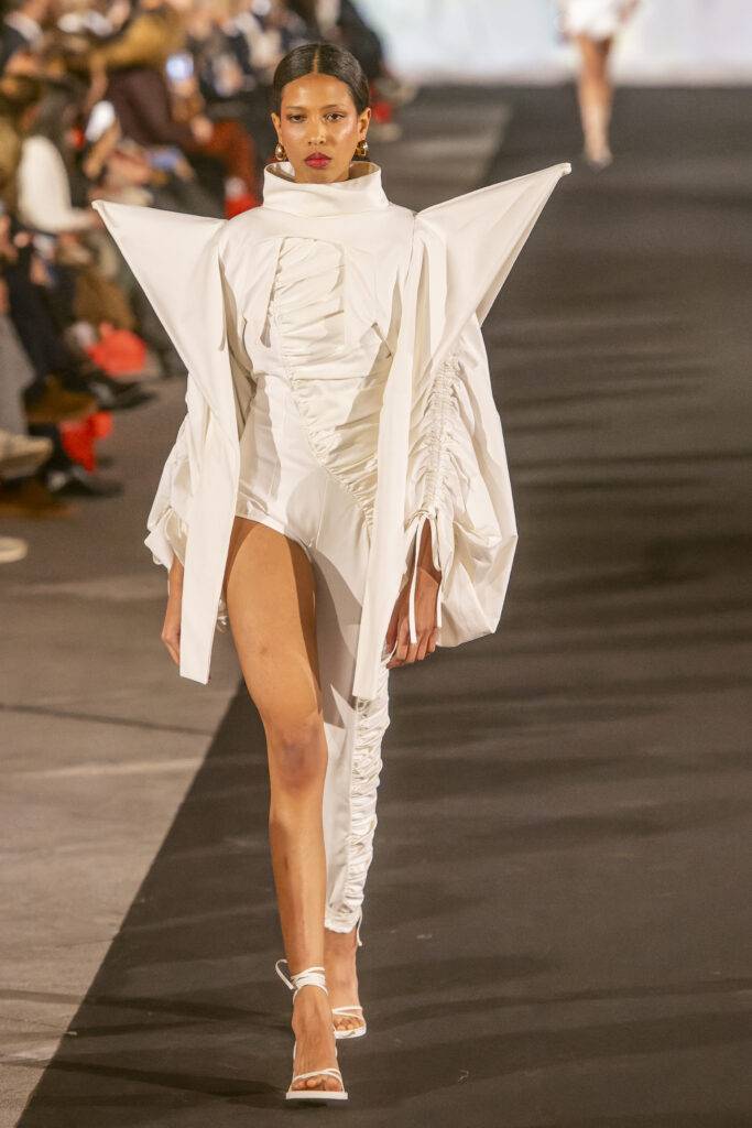 Una modelo camina por la pasarela luciendo un vestido blanco con un diseño vanguardista.