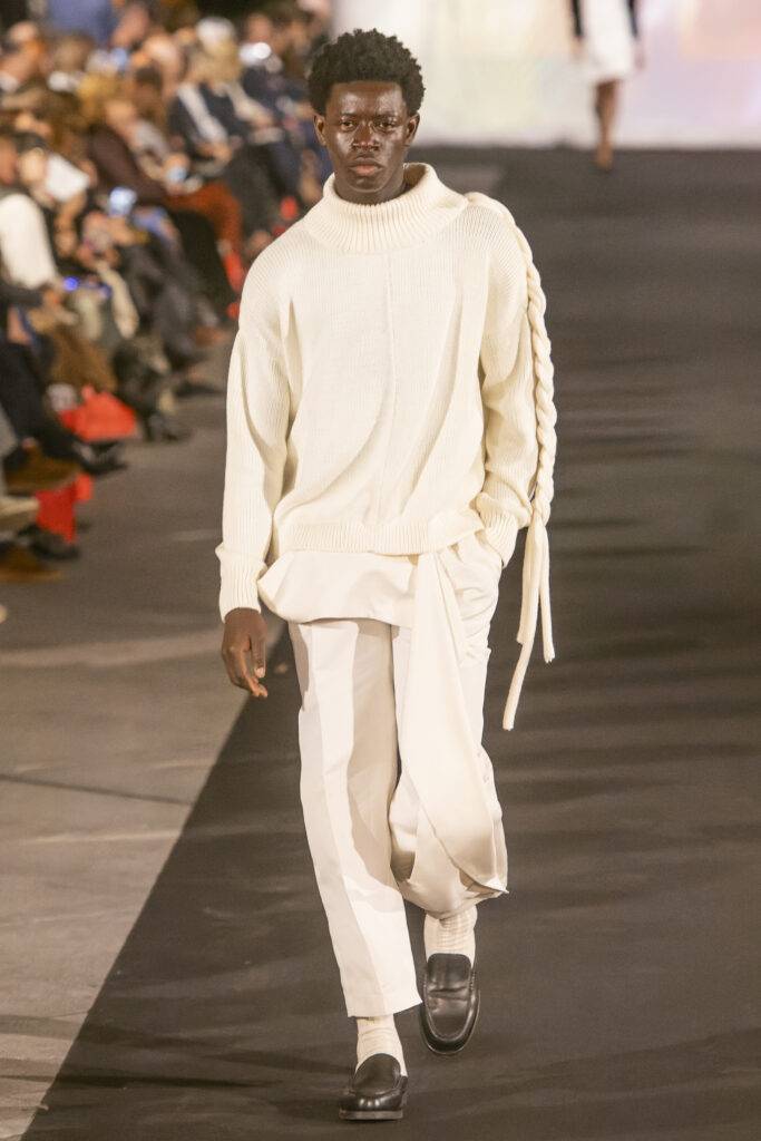 Un modelo camina sobre la pasarela vistiendo un conjunto elegante de color blanco.