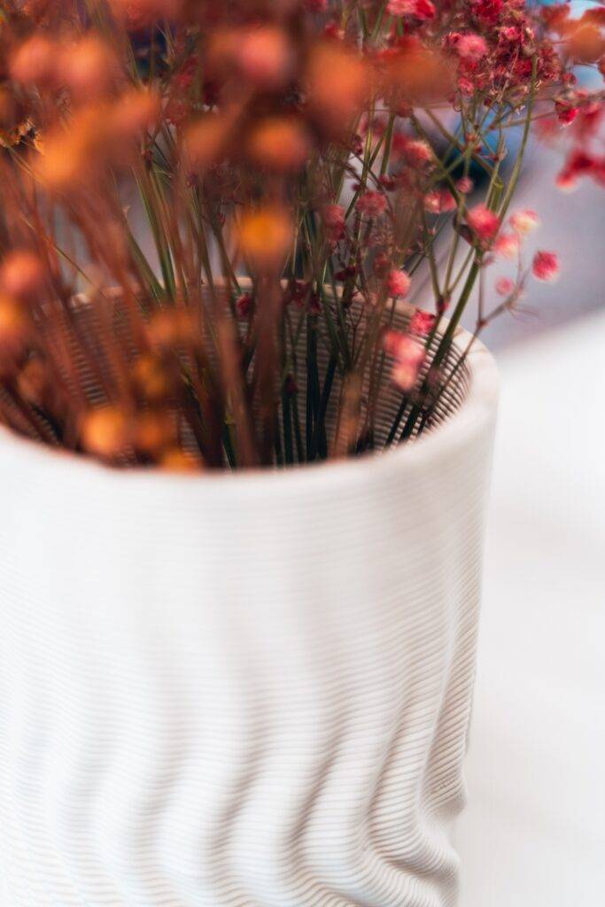 Un jarrón blanco con flores secas de colores vibrantes.