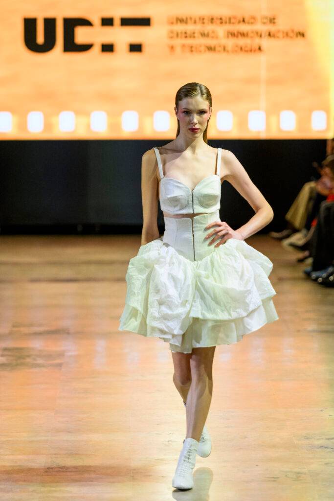 Una modelo desfila con un vestido blanco en un evento de moda.