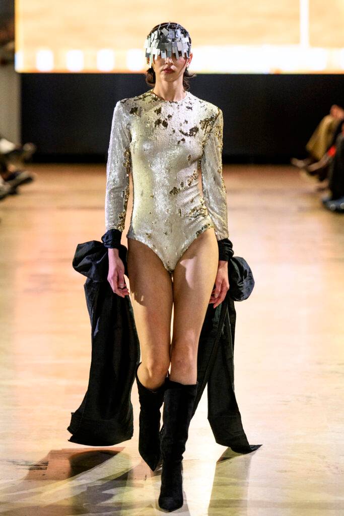 Una modelo camina por la pasarela luciendo un traje brillante y un sombrero llamativo.