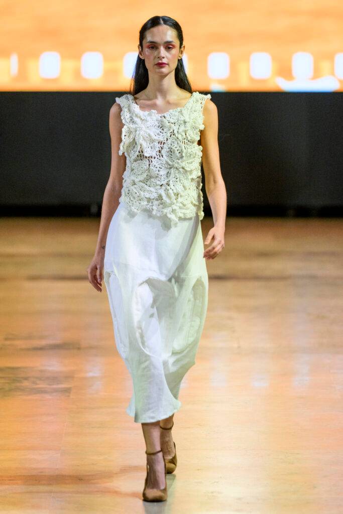 Una modelo camina por la pasarela luciendo un vestido blanco con detalles de encaje.