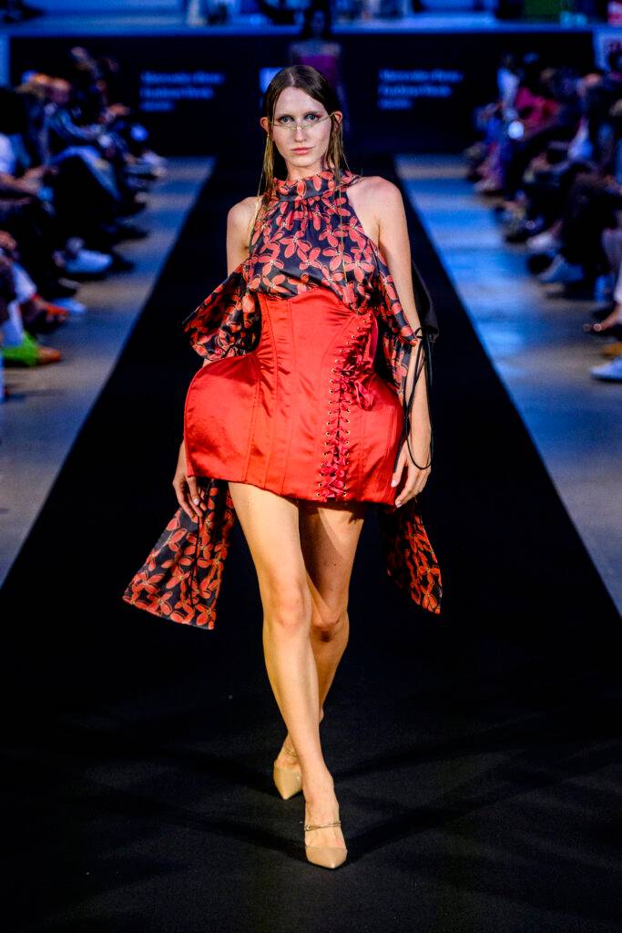 Modelo desfilando en una pasarela con un vestido rojo y detalles negros.