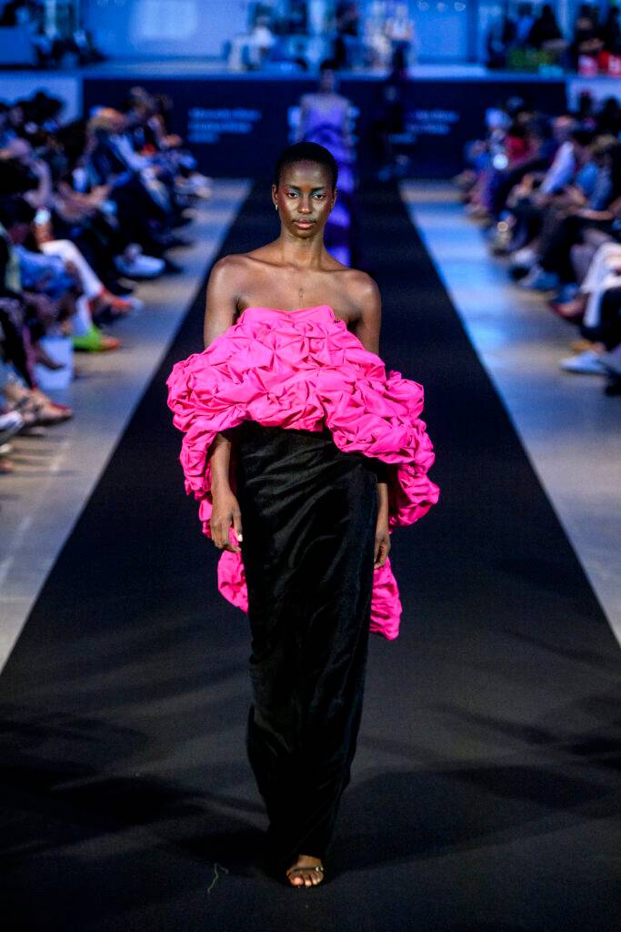 Un modelo desfila en una pasarela luciendo un vestido negro con una parte superior de volantes rosas.