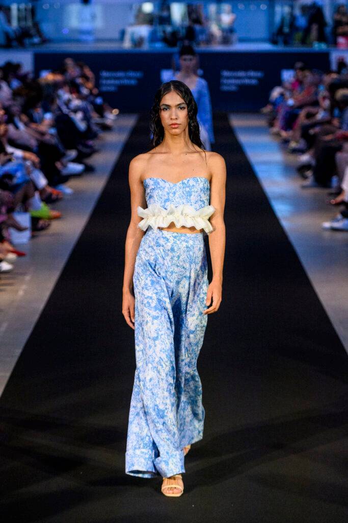 Una modelo camina por la pasarela luciendo un conjunto de dos piezas en tonos azules con un diseño floral.
