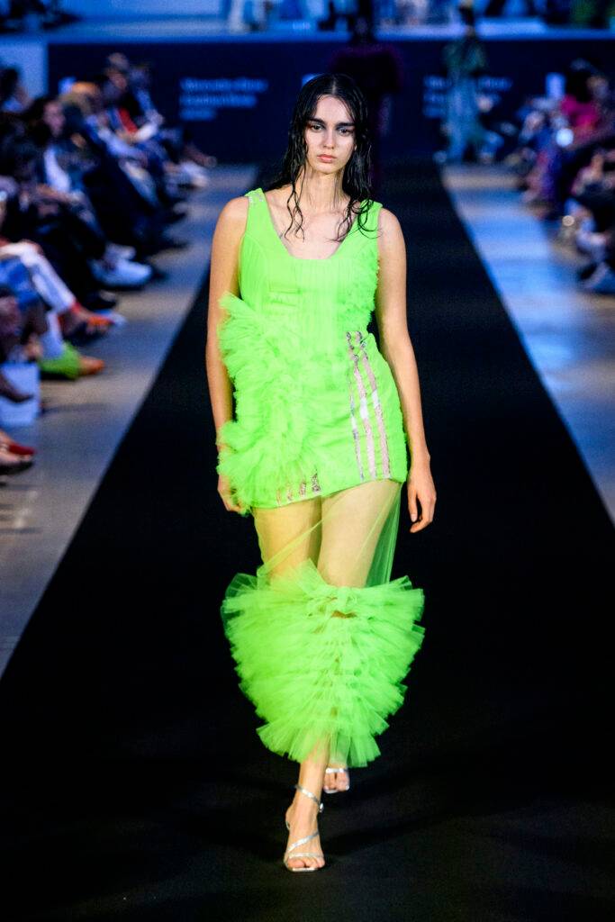 Una modelo camina por la pasarela luciendo un vestido de color verde neón con detalles de tul.