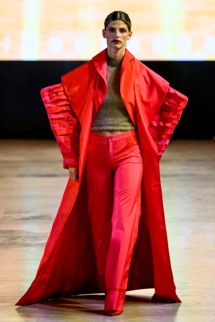 Una modelo presenta un atuendo llamativo en tonos rojos en una pasarela.
