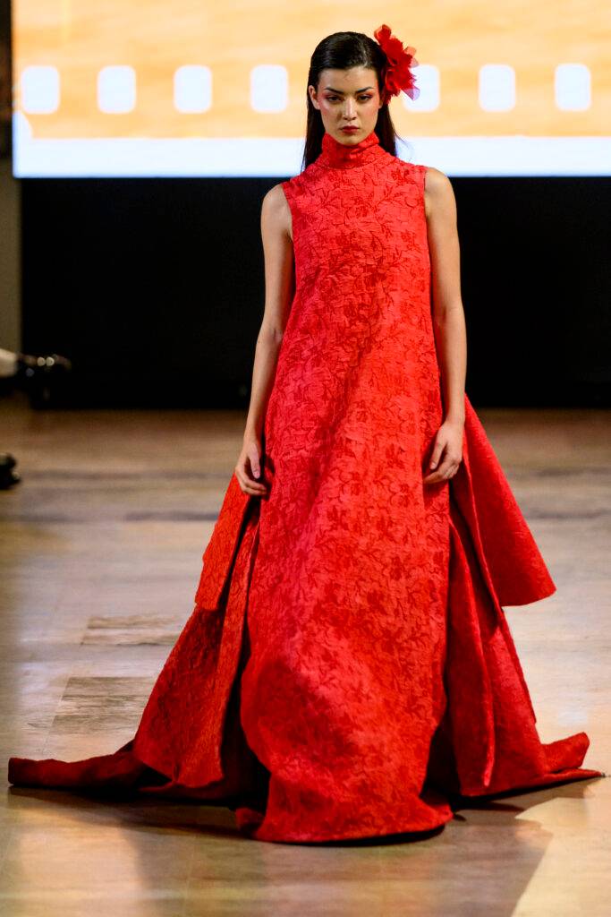 Una modelo camina en una pasarela vistiendo un vestido largo y rojo con un diseño floral.