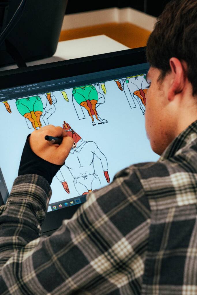 Un joven está dibujando en una pantalla digital mientras viste una camisa de cuadros.