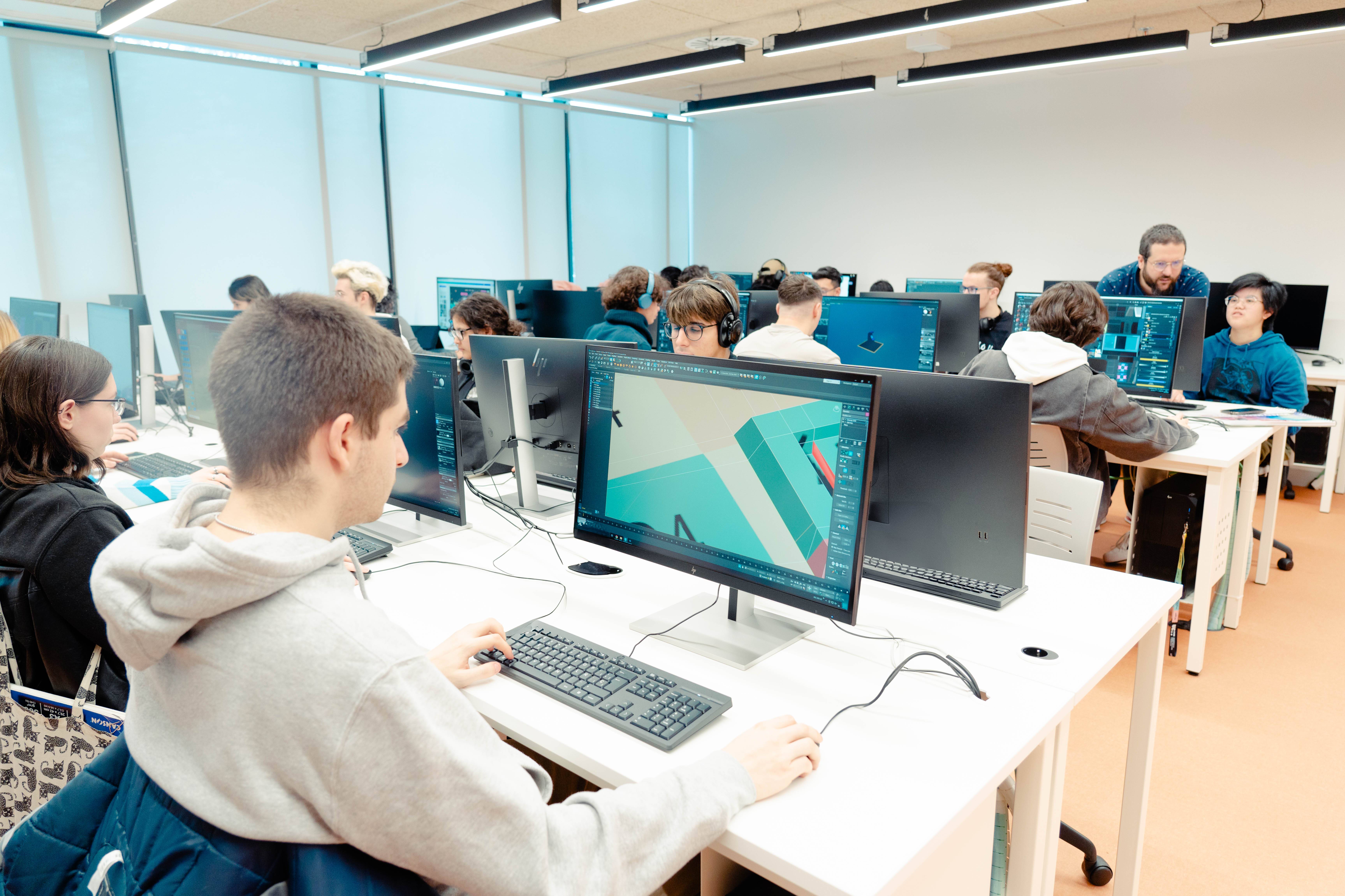 Un aula de computación con estudiantes trabajando en ordenadores mientras un profesor les dirige.