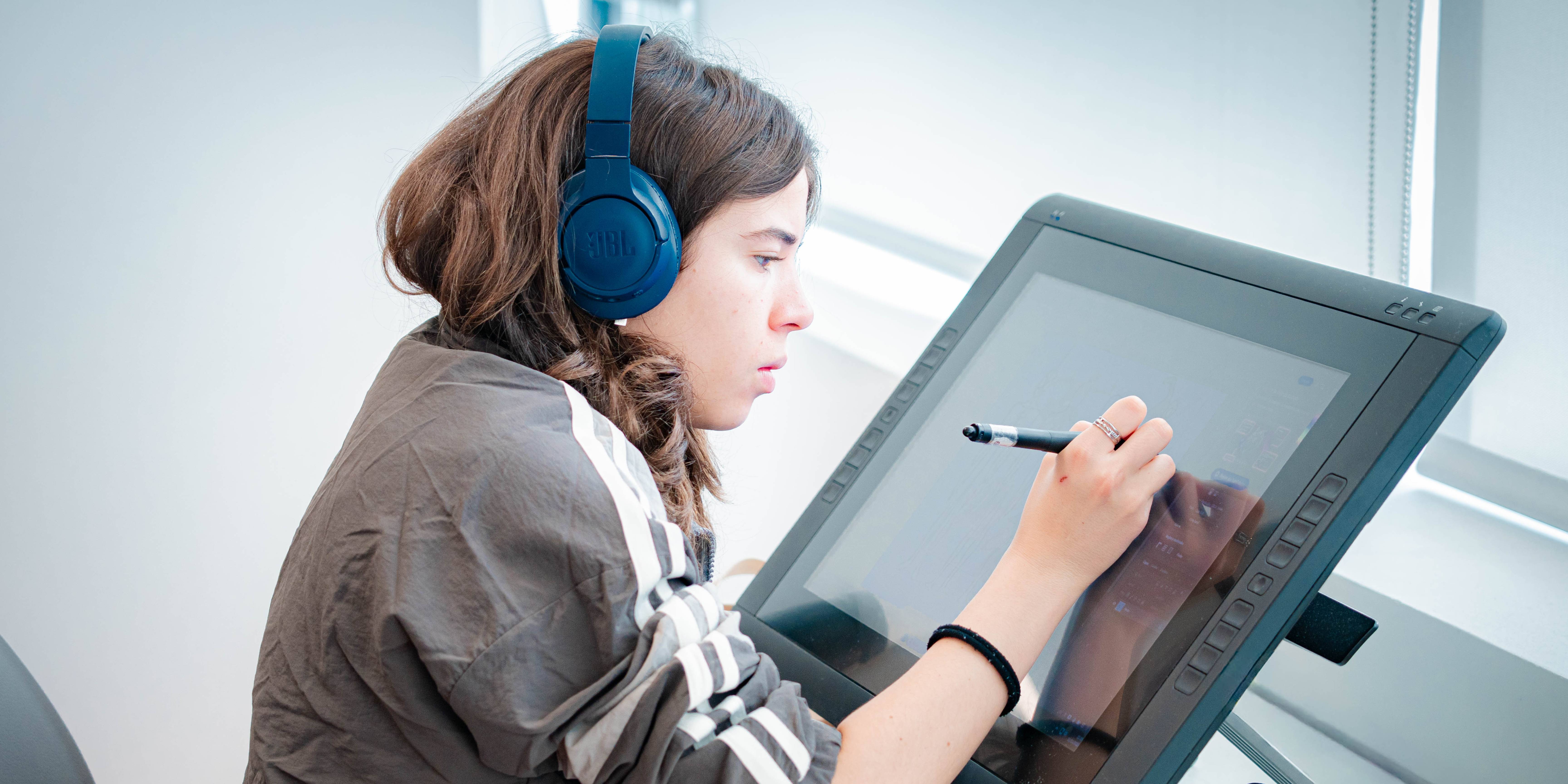 Una joven utiliza una tableta gráfica para dibujar mientras escucha música con auriculares.