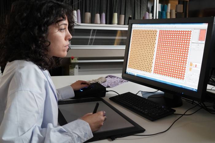 Una mujer está trabajando en un ordenador con una tableta gráfica, diseñando patrones en la pantalla.