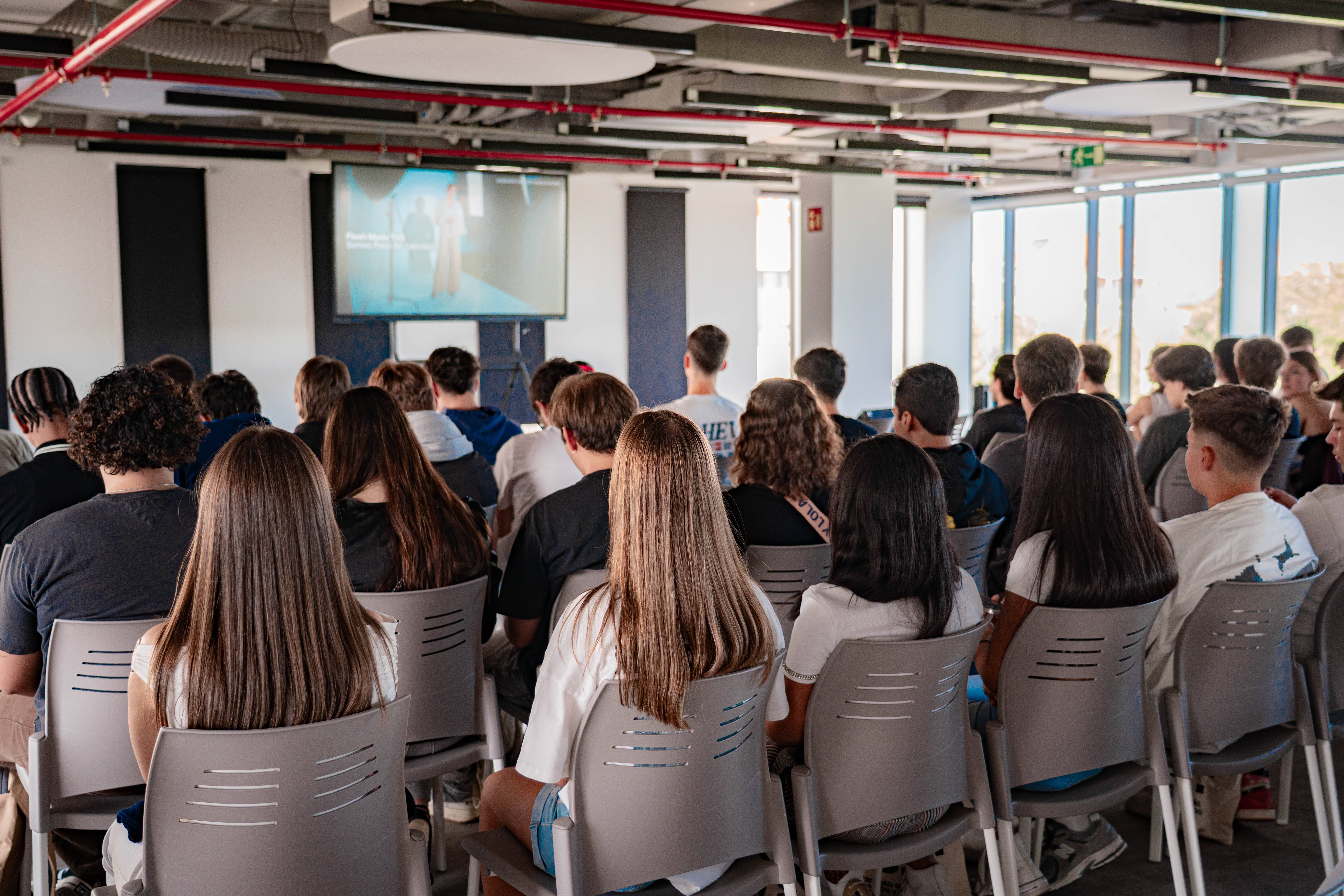 Un grupo de personas sentadas en un salón mirando una presentación en una pantalla.