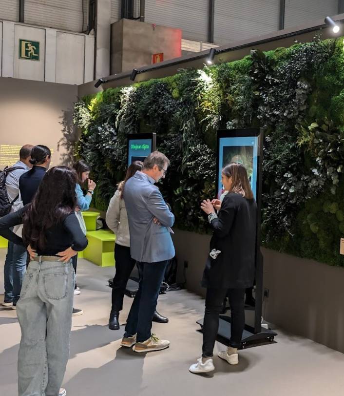 Un grupo de personas observa interactivamente paneles en un entorno con una pared verde de plantas.