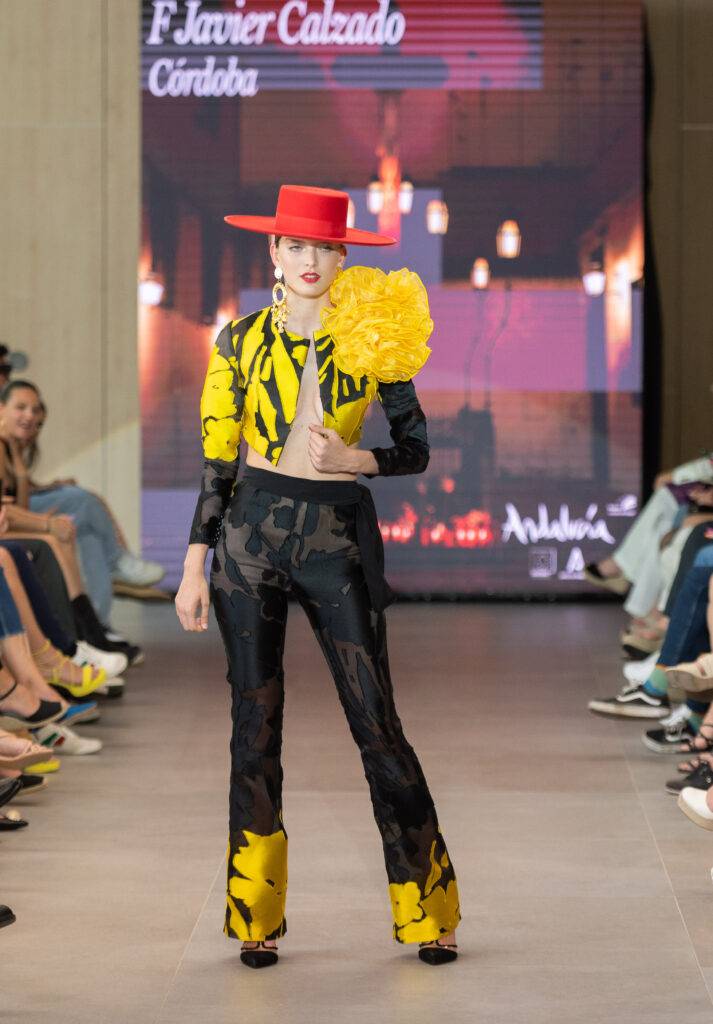 Una modelo desfilando con un conjunto de ropa colorido y un sombrero rojo en una pasarela.