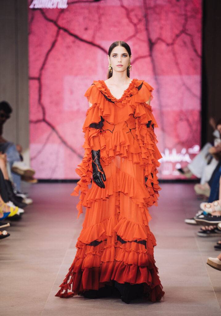 Una modelo presenta un vestido largo y rizado de color naranja en una pasarela.