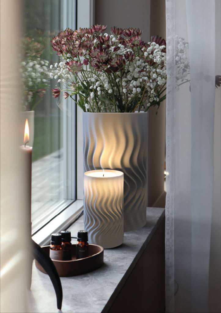 Una ventana decorada con un jarrón de flores y una vela encendida sobre una repisa.