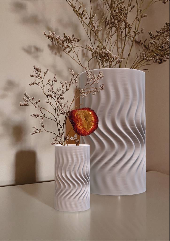 Dos jarrones blancos con un diseño ondulado, uno más pequeño que el otro, contienen ramitas secas y una rodaja de fruta deshidratada.