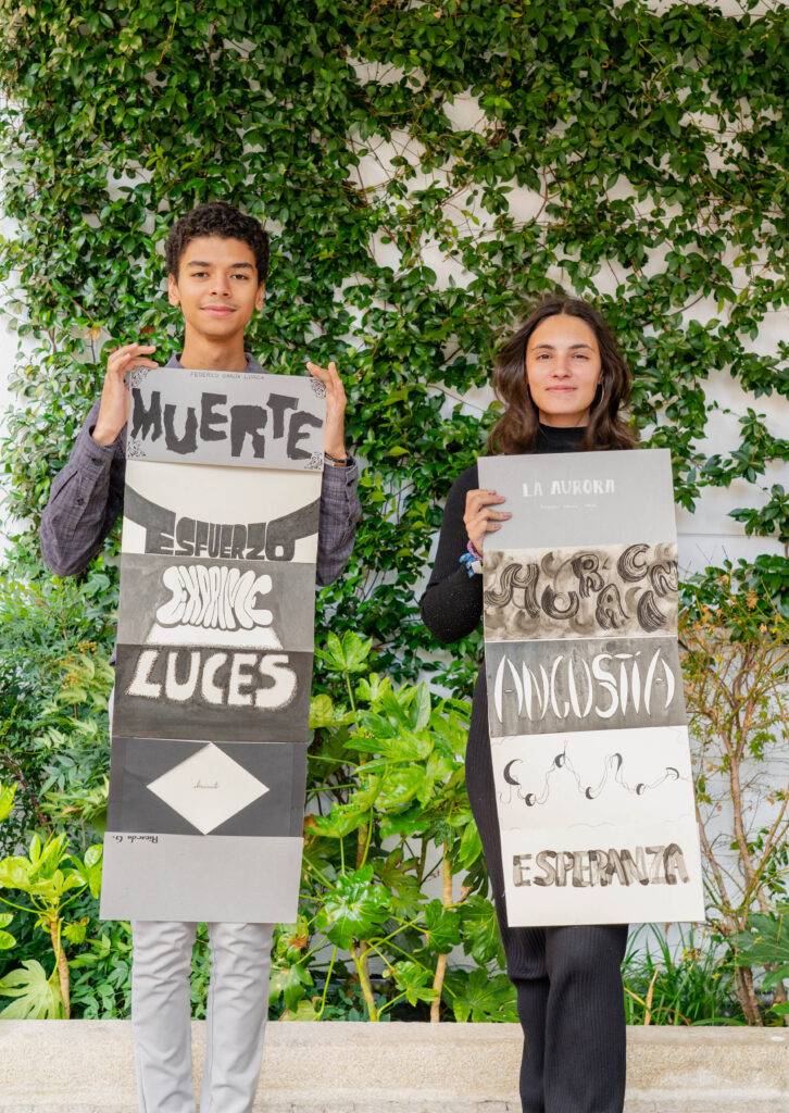 Dos jóvenes sostienen carteles con palabras en un entorno natural.