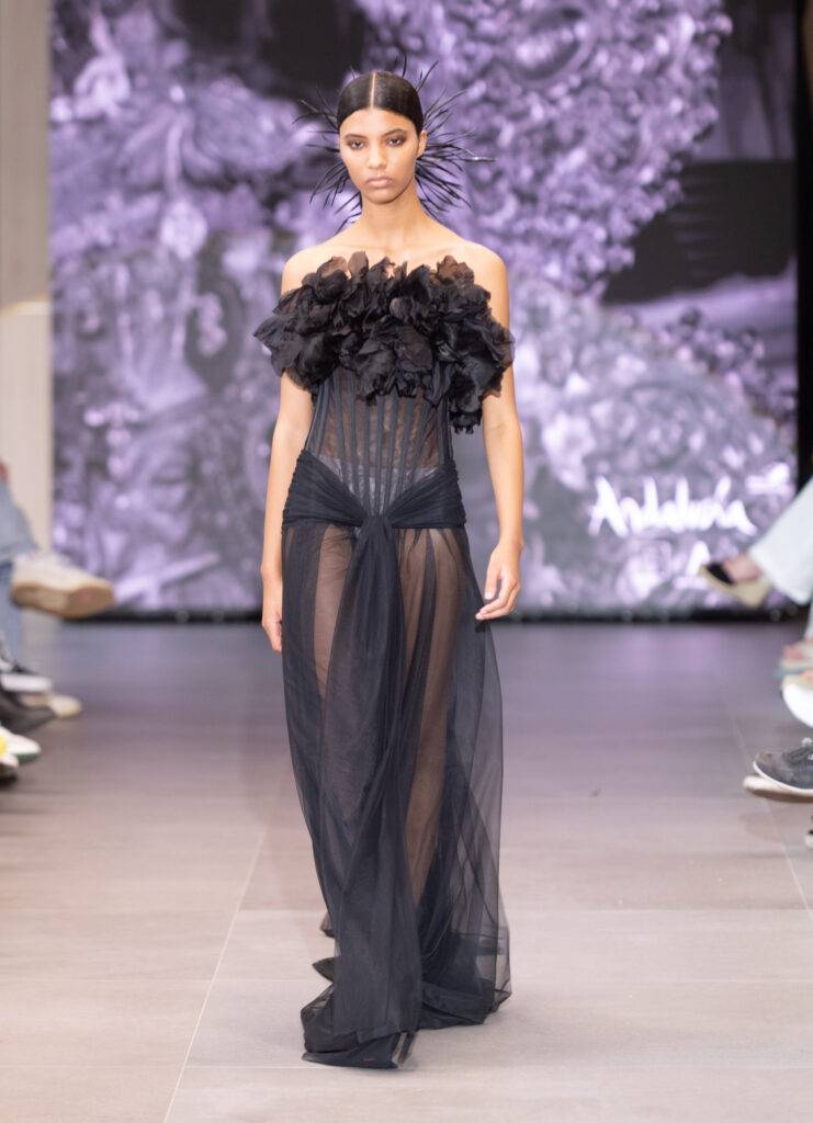 Una modelo camina por la pasarela luciendo un vestido negro transparente con volantes.