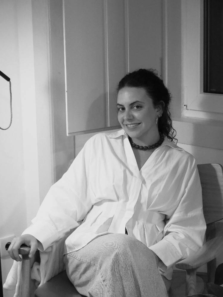 Una mujer sonriente lleva una camisa blanca y está sentada en una silla.