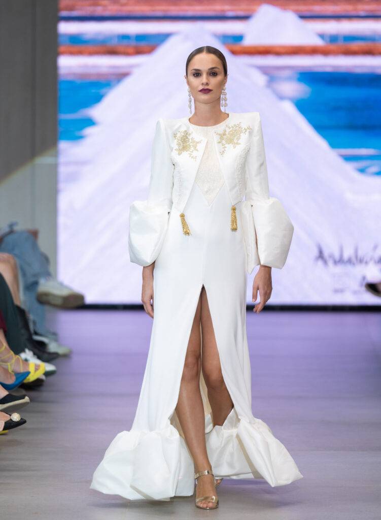 Modelo luciendo un vestido blanco con detalles elegantes en una pasarela de moda.