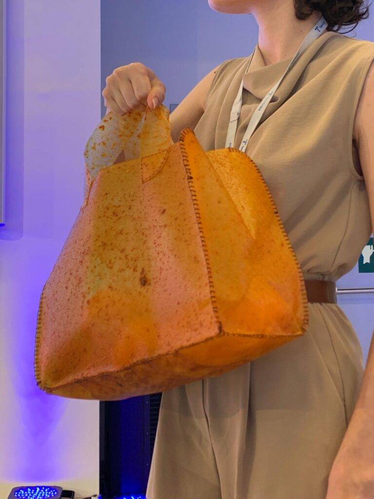Una mujer sostiene un bolso de color naranja que parece estar hecho de material reciclado.