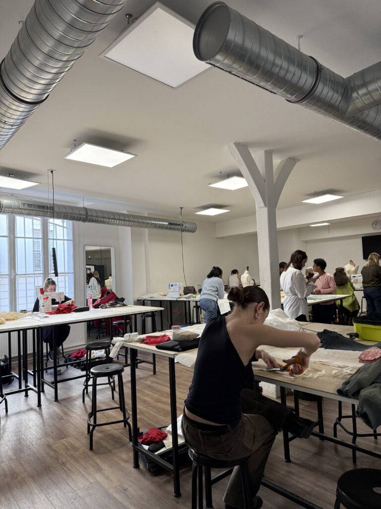 Un taller de costura con varias personas trabajando en sus proyectos en un ambiente luminoso y organizado.