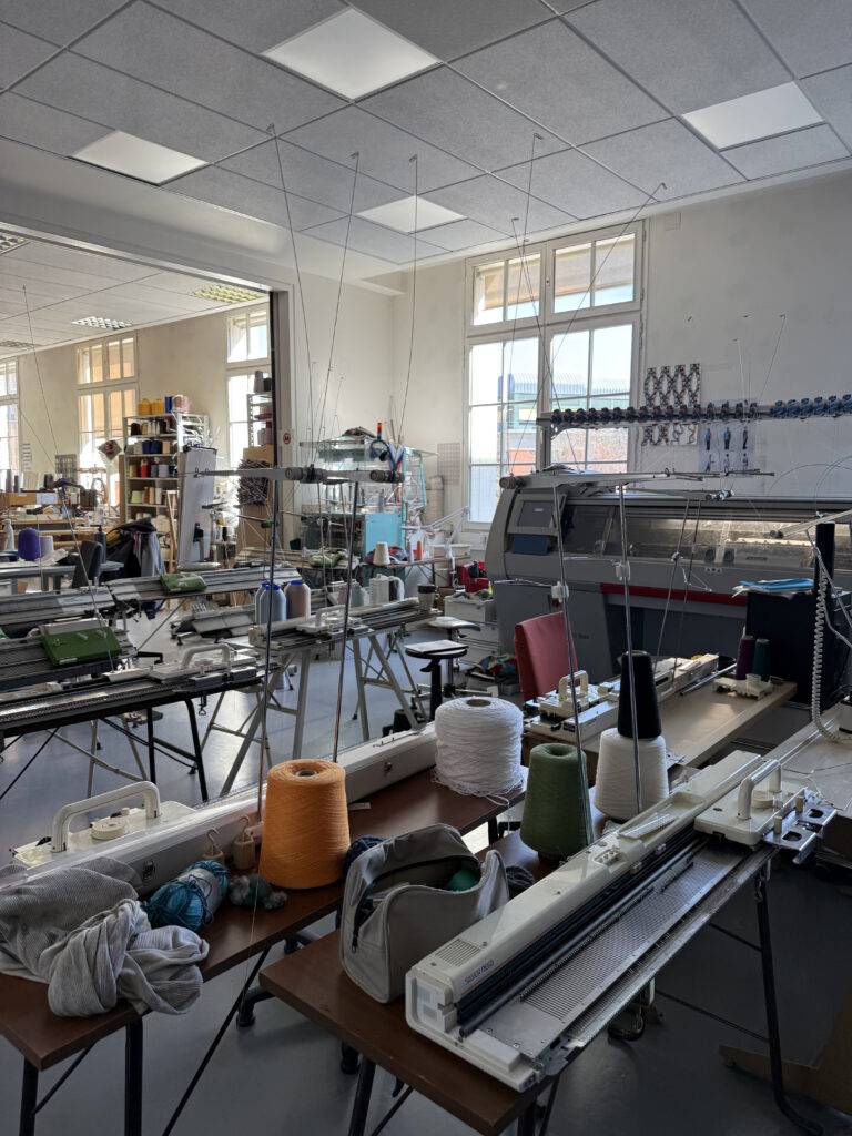 Un taller de confección textil con máquinas de tejer y hilos en mesas desordenadas.