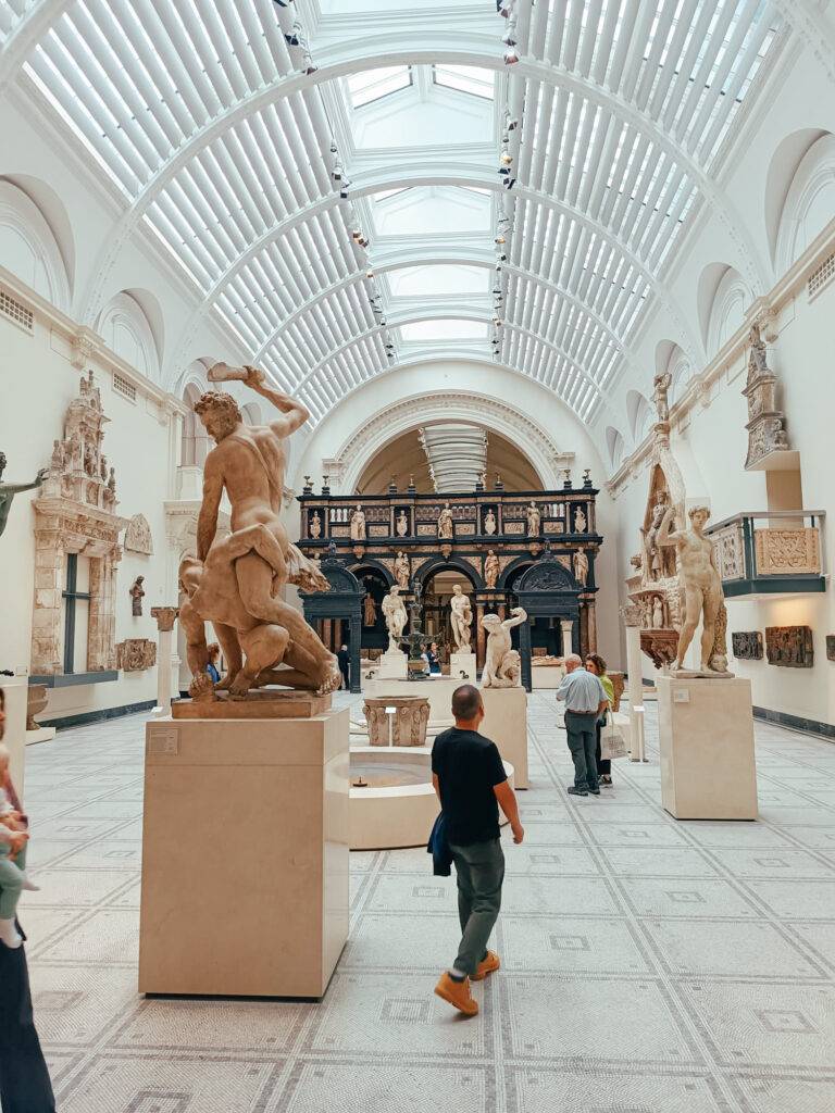 Una sala amplia de museo con varias esculturas y visitantes admirando las obras.