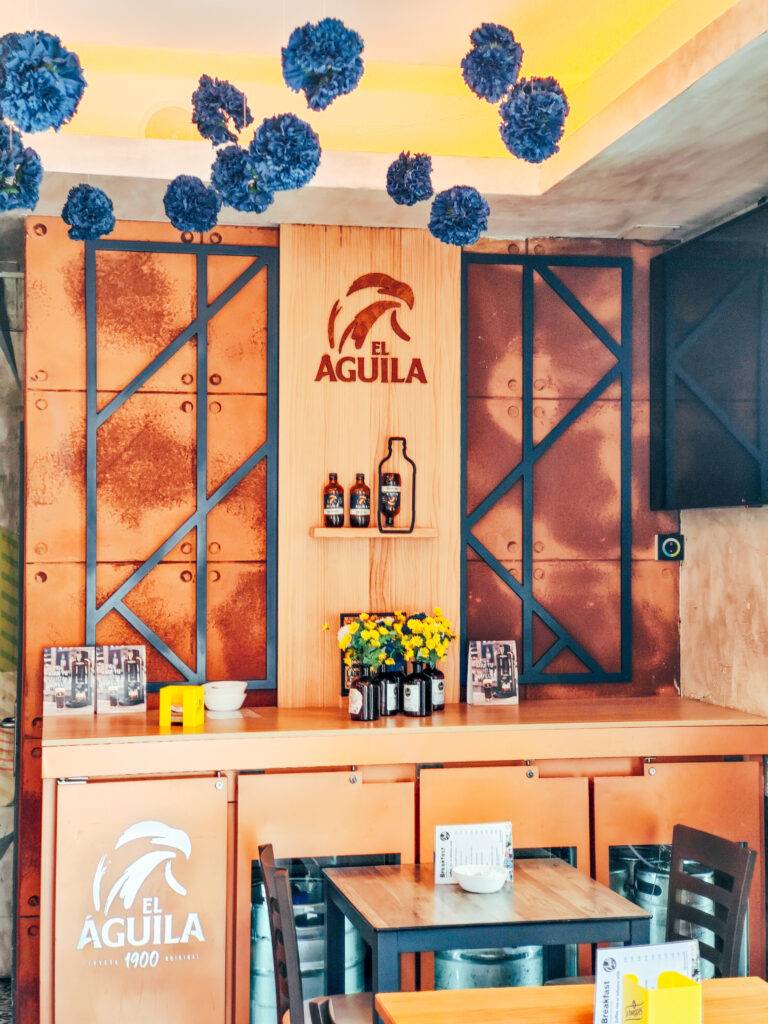 Interior de una barra de bar decorada con elementos industriales y el logotipo de El Águila.