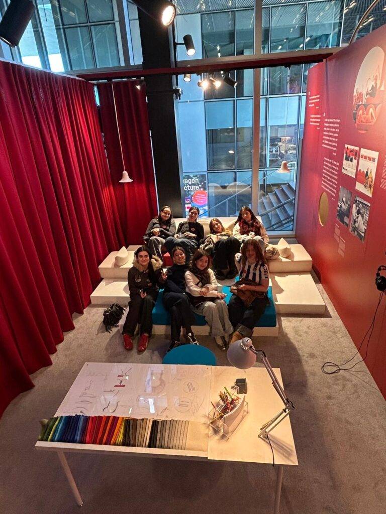 Un grupo de personas se relaja en un salón con paredes rojas y muebles de colores en un ambiente moderno.