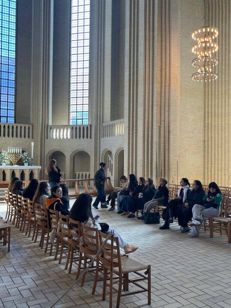Un grupo de personas sentadas en un interior de iglesia con altos ventanales.
