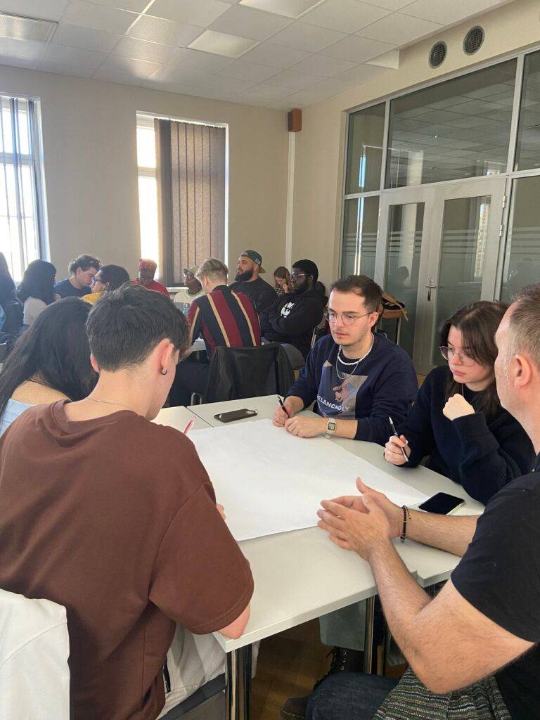 Un grupo de personas en una sala, trabajando en equipo alrededor de una mesa.